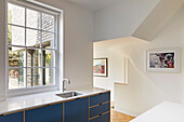 Blue kitchen cabinets under the mullioned window and angled hallway