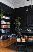 Bookshelf and houseplant in front of black wall in the corner of room