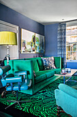 Green sofa, vintage leather chair and carpet with malachite pattern in the living room with blue walls