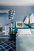 Queen bed, model sailboat above, bedside lamp with oversized lampshade in a bedroom