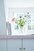 Books and flower vase on wide windowsill, storage cabinets underneath