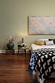 Textilbild an grün getönter Wand über Doppelbett im Schlafzimmer