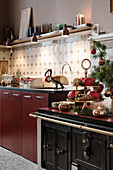 Antique stove and oven next to dark red kitchen cabinet, tiled backsplash, and shelf above it
