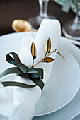 White place setting with green decorative ribbon as napkin ring and golden branch