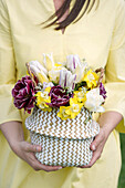 Frau in gelbem Kleid hält einen Korb mit bunten Frühlingsblumen