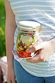 Preserving jar with fresh salad and fork in the hand of a person outdoors