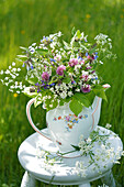 Hocker mit Wildblumenstrauß aus  Beinwell, Giersch, Rotklee (Trifolium pratense) und Wiesensalbei in alter Teekanne