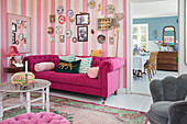 Pink sofa, photos and decorative plates hung on the wall in a lounge with pink striped wallpaper