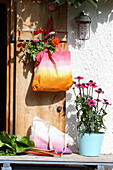 Colorful DIY fabric bag with dahlias on a wooden door, in front of it purple coneflower in a pot