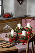 Advent wreath with greenery, red ribbon decorations and biscuits on a rustic table