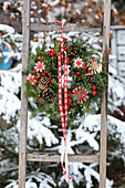 Winter door wreath made from fir branches, straw stars and red berries on a wooden ladder