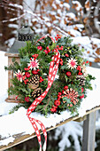 Winter door wreath made from fir branches, cones and red berries outside in the snow
