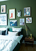Double bed below gallery of pictures on green wall