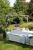 Gedeckter Sommertisch mit Rittersporn und Kletterrosen im sonnigen Garten