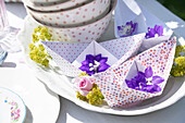 Papierboote mit Ritterspornblüten auf Teller, Tischdeko