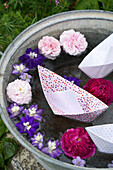 Ritterspornblüten, Rosenblüten und Papierboote als Schwimmdeko in einer Zinkwanne