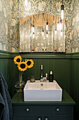 Aufsatzbecken auf grüner Kommode, darüber Spiegel und Tapete in Gäste-Toilette