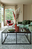 A coffee table with ornamental grasses and a green upholstered sofa in a lounge