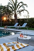 Beistelltisch mit Drinks und Sonennliegen am Pool beim Sonnenuntergang