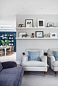 Light upholstered armchairs, above shelves with photos and decorative objects
