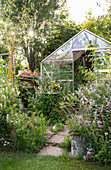 Gewächshaus in sommerlichem Garten mit üppiger Bepflanzung