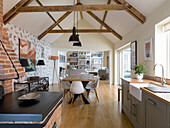 Moderne Landhausküche mit Holzbalken und Holzofen aus rustikalen Ziegelsteinen, im Hintergrund Ess- und Wohnbereich