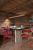 Wooden table with black tabletop and red chairs in the dining area of a wooden hut
