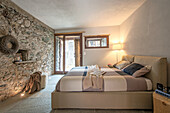 Comfortable king size bed in the illuminated bedroom with natural stone wall