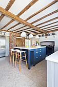 Central unit with blue fronts in open-plan kitchen with wood-beamed ceiling
