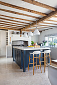 Center kitchen island with blue fronts in open plan kitchen with wood-beamed ceiling
