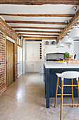 Mittelblock mit blauen Fronten in offener Küche mit Backsteinwand und Holzbalkendecke