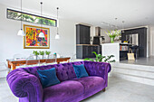 Purple Chesterfield sofa with velvet upholstery in light, open-plan living room with stone tiles