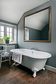 Oversized mirror on a blue grey wall above a claw foot bathtub