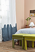 Two upholstered stools and floor-length curtains in a bedroom