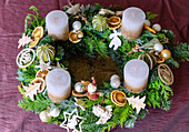 Mit Naturschmuck, Holzschmuck und Blechfiguren dekorierter Adventskranz aus gemischten Tannen- und Koniferenzweigen und goldweißen Kerzen