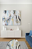 Weißes Sideboard, darüber moderne Kunst in hellem Wohnzimmer