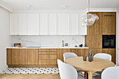 Fitted kitchen with white wall unit and wooden fronts, round dining table in the foreground
