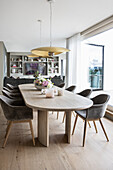 Long dining table in light wood with elegant, upholstered shell chairs in front of patio door