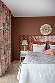 Double bed with high headboard and matching pillows in the bedroom in warm red tones
