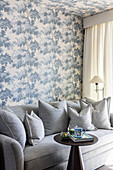 Light grey upholstered sofa in front of a wall with wallpaper with tree motif in blue tones