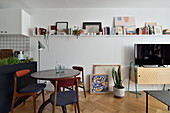 Small dining area with vintage chairs and TV cabinet, shelf with pictures and books