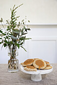 Frisch gebackene Kekse auf Tortenplatte aus Marmor und Vase mit Blätterzweigen