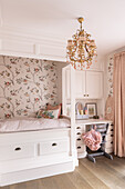 White four-poster bed with bird wallpaper and small writing desk in the girls' room in shades of pink