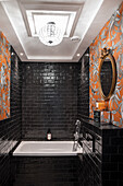 Badewanne im Badezimmer mit schwarzen Wandfliesen und Tapete in Orangetönen