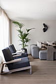 Designer armchair, indoor palm tree and upholstered sofa with throw pillows in light living room