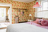 Pink cushions and crocheted bedspread on double bed in bedroom with floral wallpaper