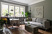 Grey upholstered sofa, concrete block as coffee table and dining area in front of window in open-plan living room