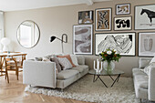 Light sofas, glass table and pictures on beige-coloured wall in open-plan living room