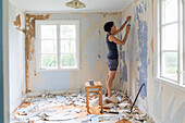 Woman renovating room and removing wallpaper