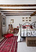 Double bed and vintage ladder as decoration in a white bedroom with rustic wooden beams